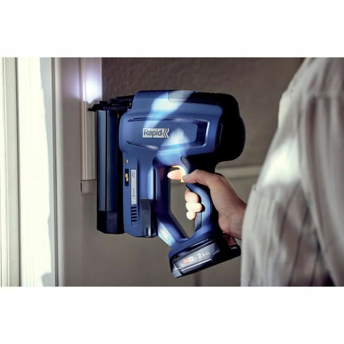 Una mano tiene una sparachiodi a batteria blu Rapid contro uno stipite.