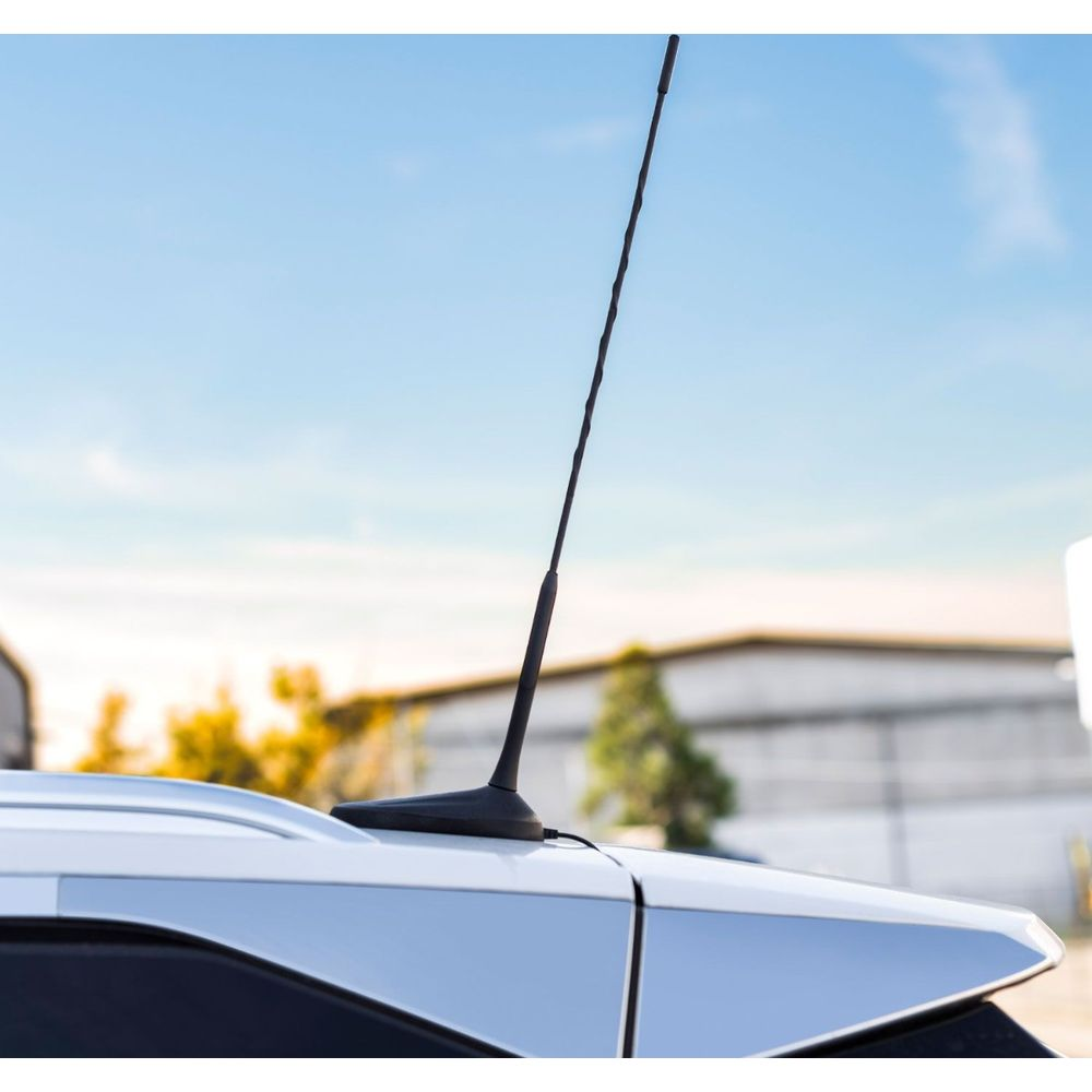Eine schwarze Antenne auf dem Dach eines weißen Autos, blauer Himmel.