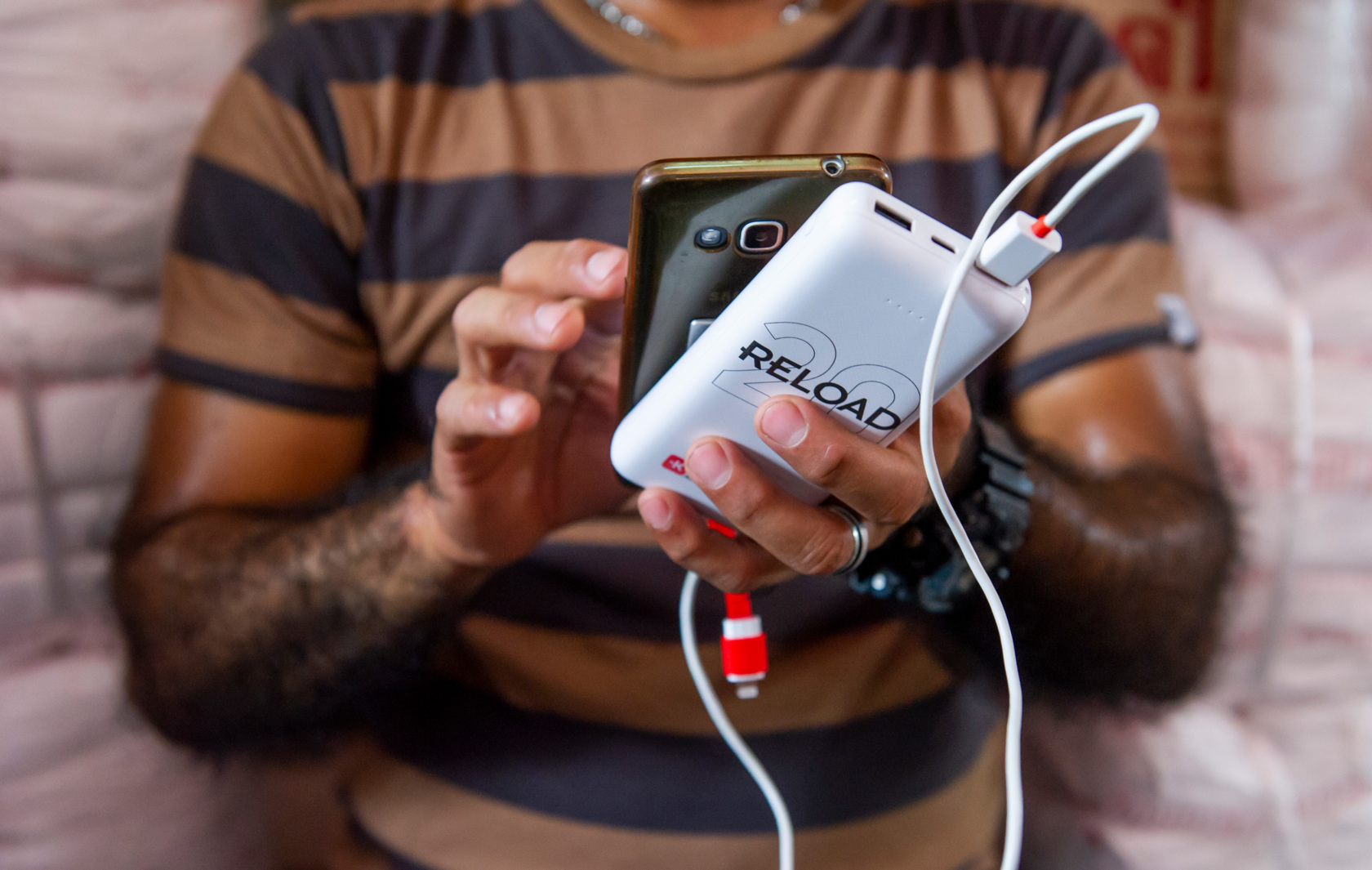 Une personne tient un smartphone et une banque d'alimentation blanche reliés par un câble.