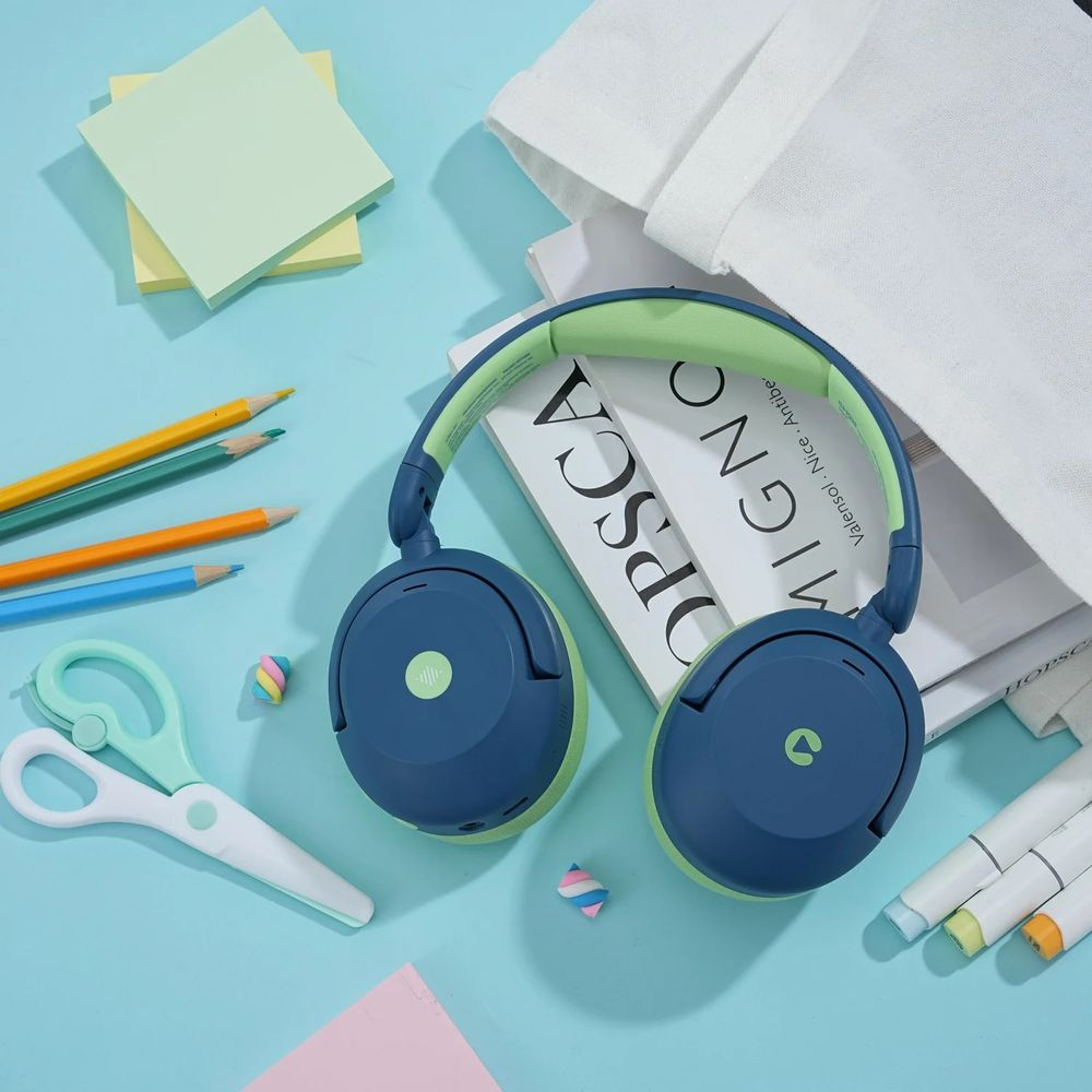 Casque bleu et vert posé sur des livres, avec crayons, ciseaux et post-it à proximité.