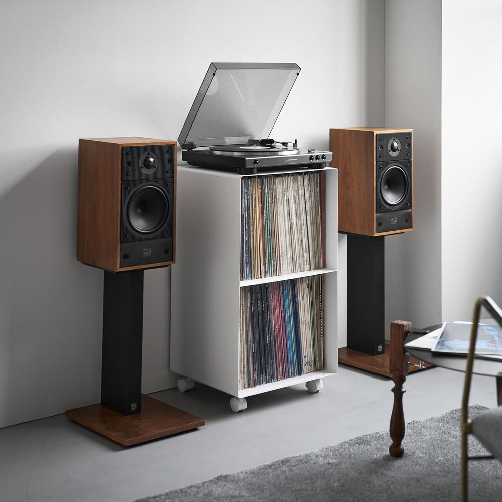 Holz-Lautsprecher auf Ständern, Plattenspieler auf weißem Regal mit Schallplatten.