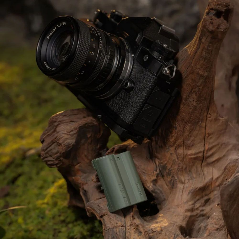 Una fotocamera nera con obiettivo e batteria verde poggiano sul legno.