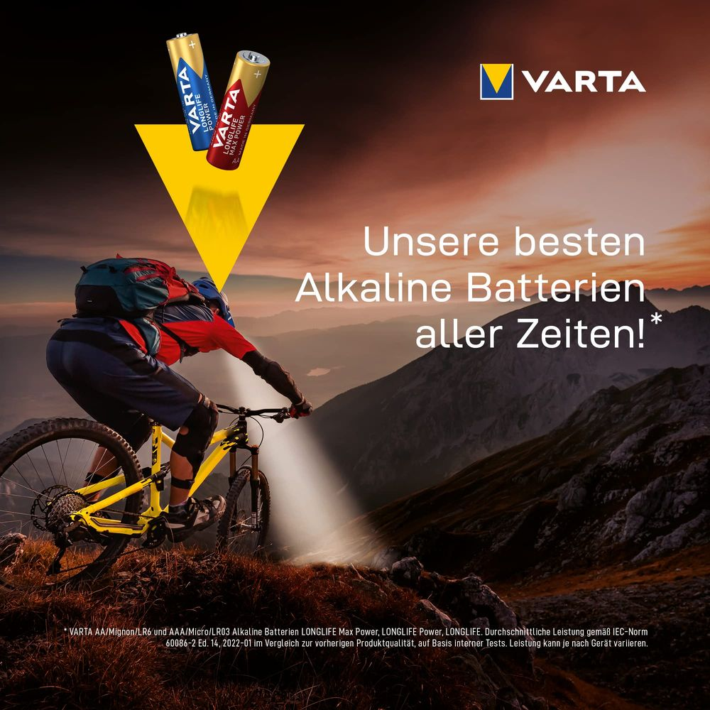 Un ciclista de montaña desciende, pilas Varta y montañas al fondo.