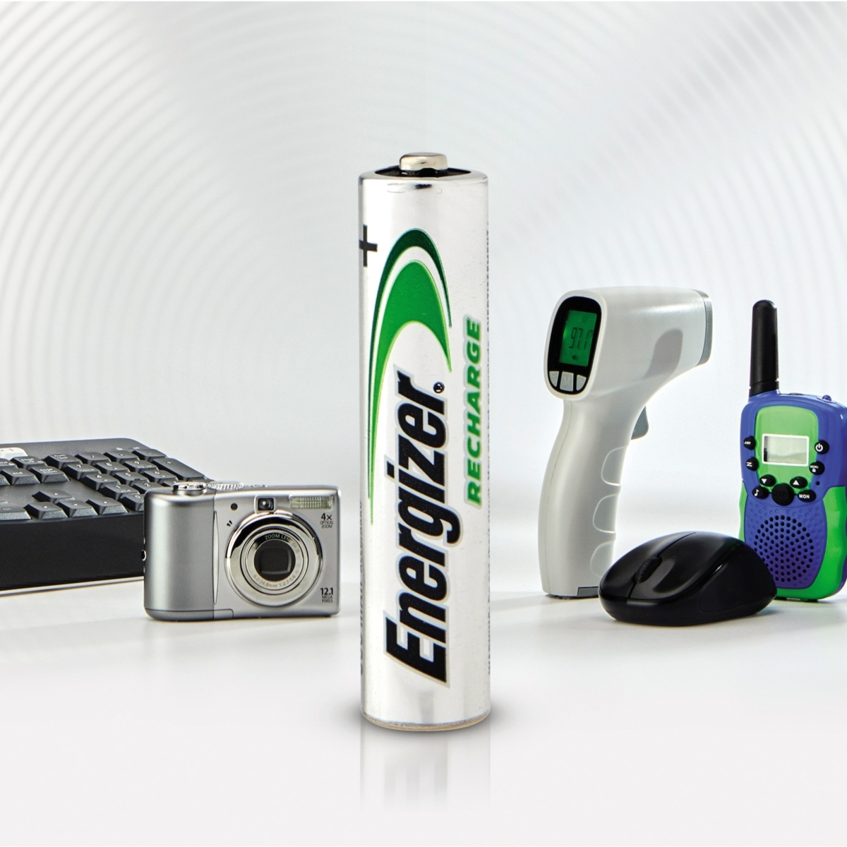 Una batteria Energizer in primo piano, con fotocamera digitale, tastiera, mouse e walkie-talkie.