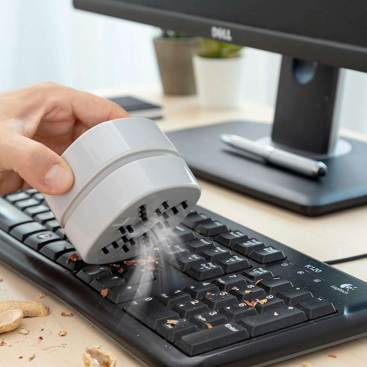 Eine Hand hält einen grauen Mini-Staubsauger über einer verschmutzten Tastatur.