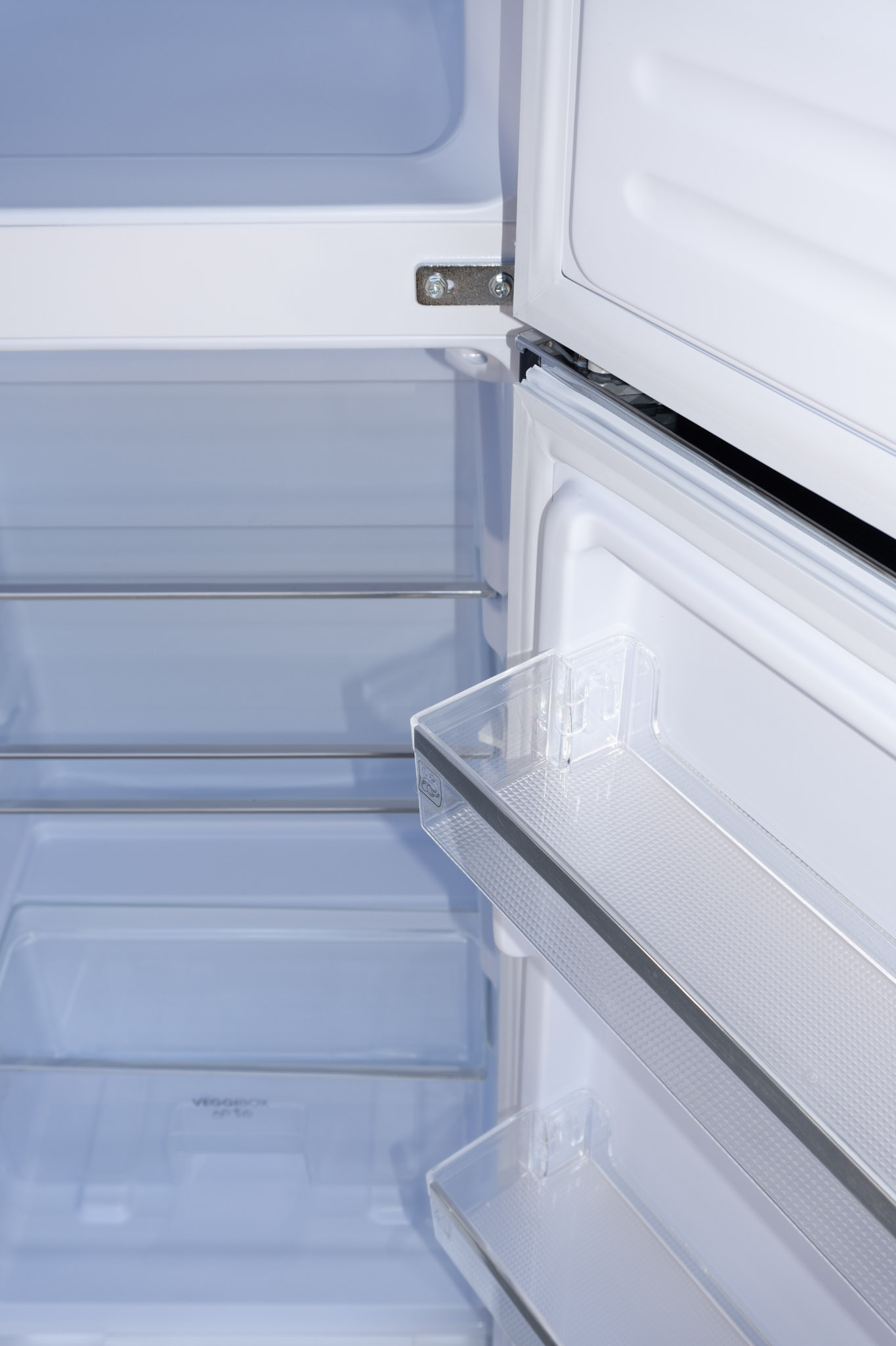 Vue intérieure d'un réfrigérateur vide avec étagères transparentes et grilles blanches.