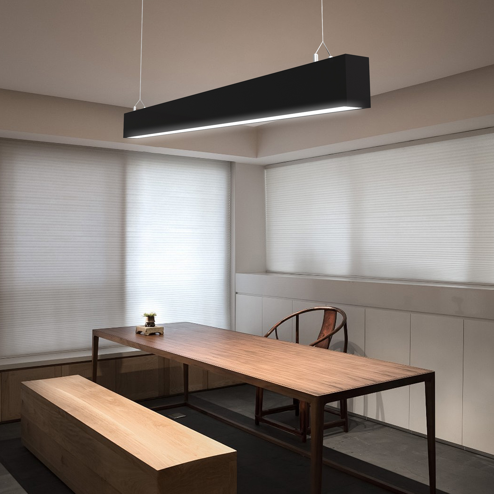 Una lámpara negra larga cuelga sobre una mesa y banco de madera.