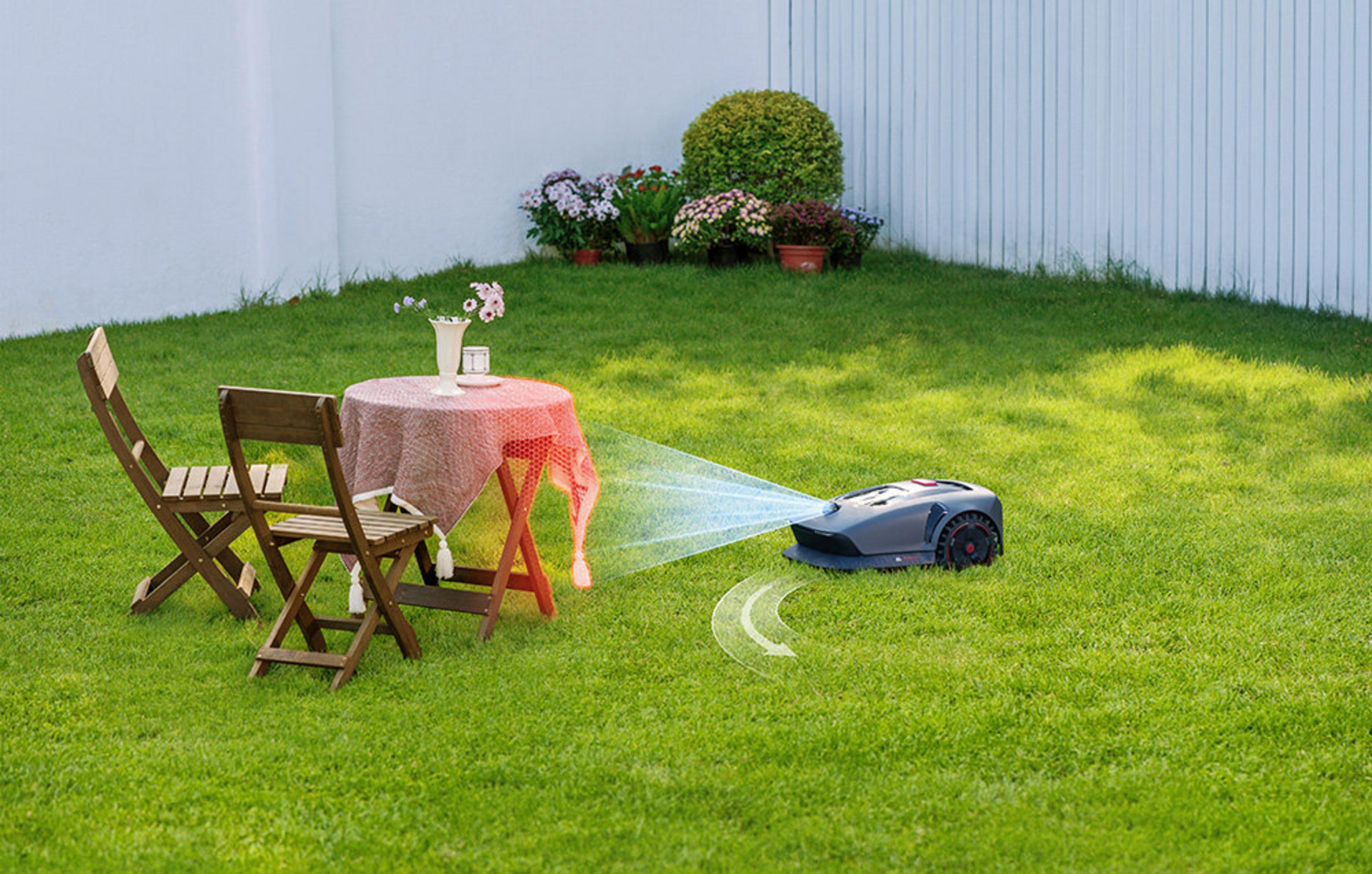 Robot koszący trawę na zielonym trawniku obok stolika ogrodowego z kwiatami.