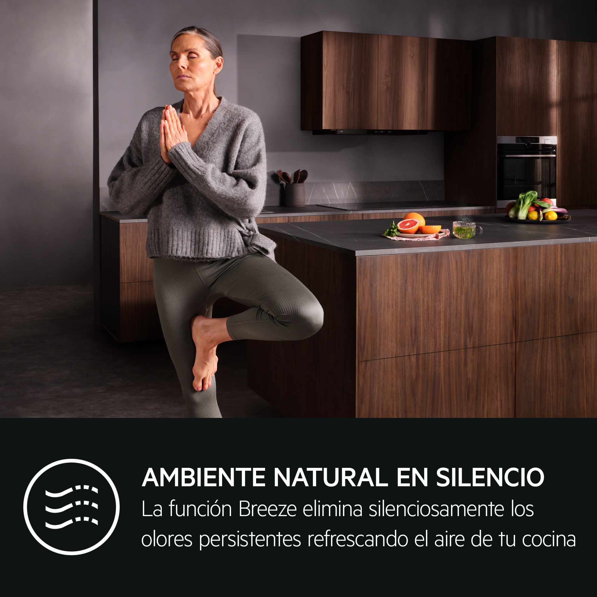 Donna in abiti grigi pratica yoga in una cucina moderna con mobili in legno.