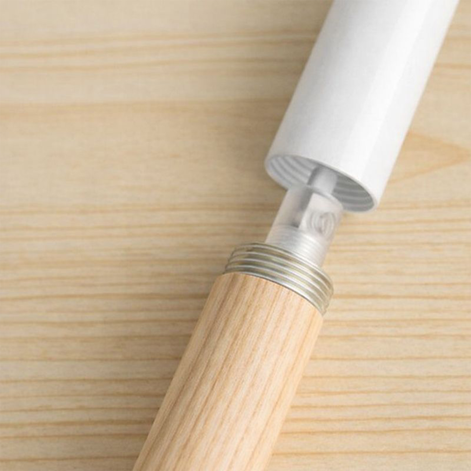 Una varilla blanca con mango de madera y rosca sobre fondo de madera.
