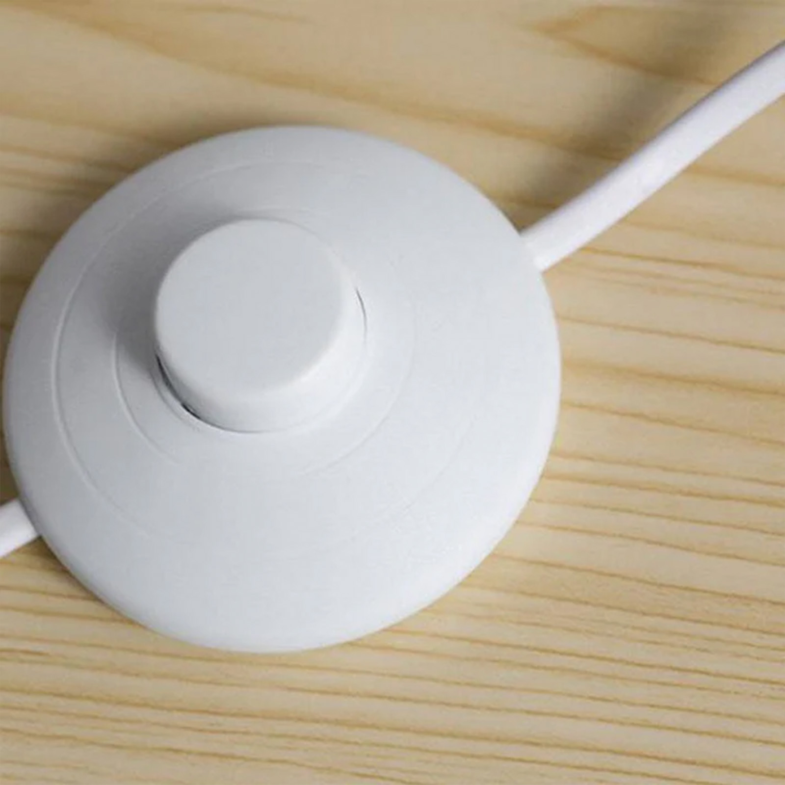 Un interruptor de pie blanco con cable sobre una superficie de madera.