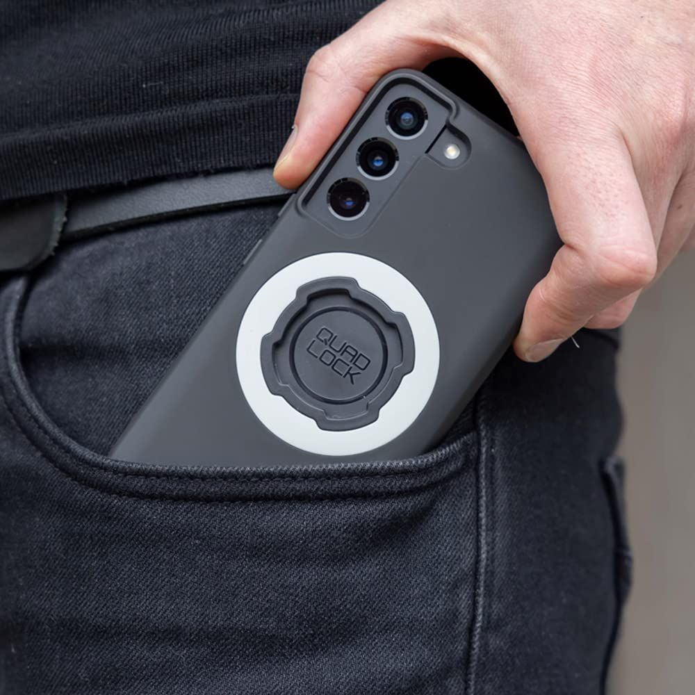 Eine Hand steckt ein dunkles Smartphone mit Quad Lock Halterung in eine Hosentasche.