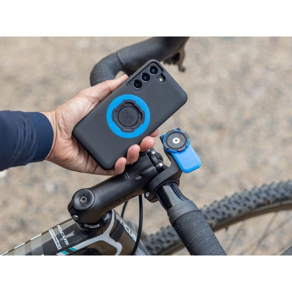 Hand hält schwarzes Handy mit blauem Ring über Fahrradlenker-Halterung.