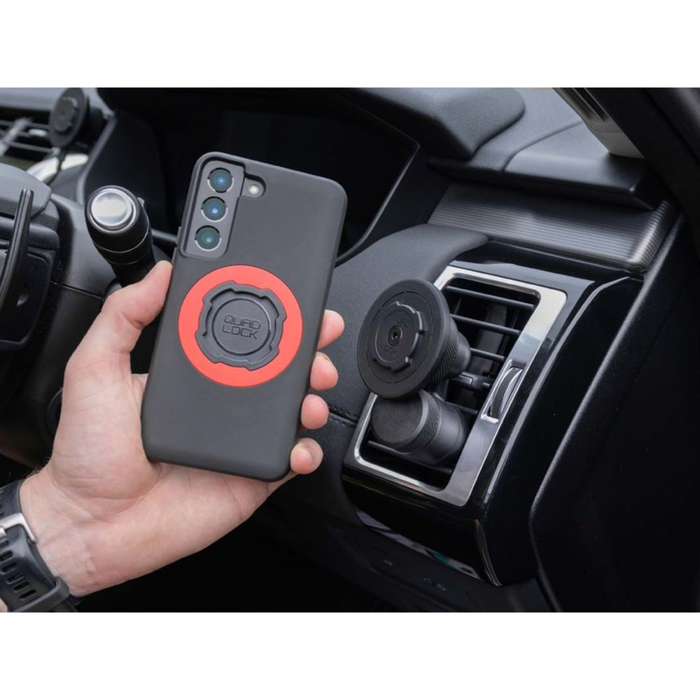Eine Hand hält ein schwarzes Handy mit rotem Ringhalter vor einem Auto-Luftauslass.