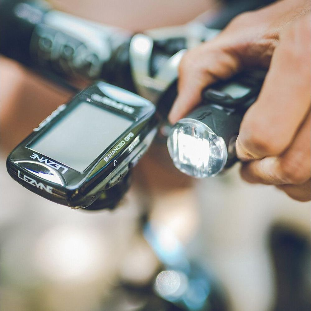 Ein Mann hält eine Fahrradlampe neben einem GPS-Gerät am Lenker.