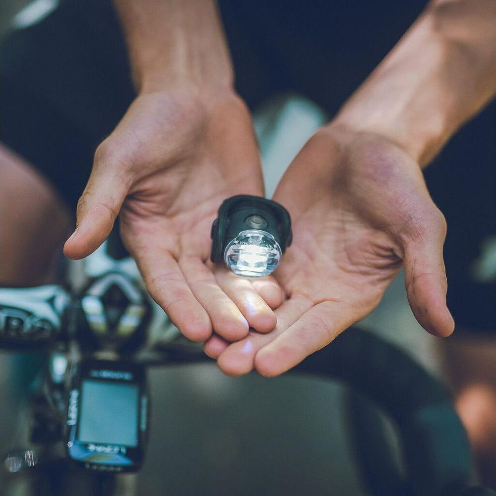 Hände halten eine leuchtende Fahrradlampe über einem Fahrradcomputer.
