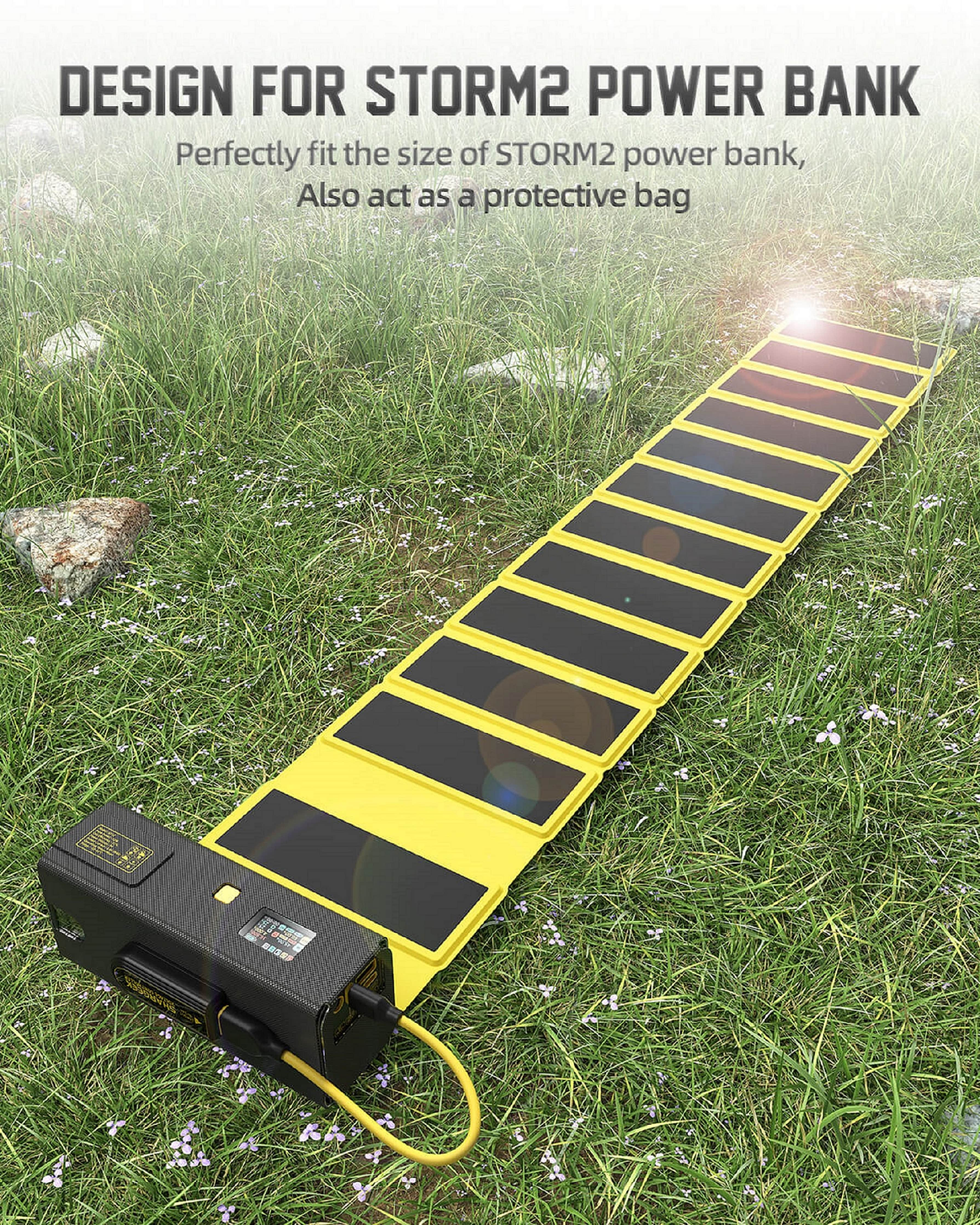Ein schwarzer Akku ist mit einem gelben, aufklappbaren Solarpanel verbunden, das auf Gras liegt.