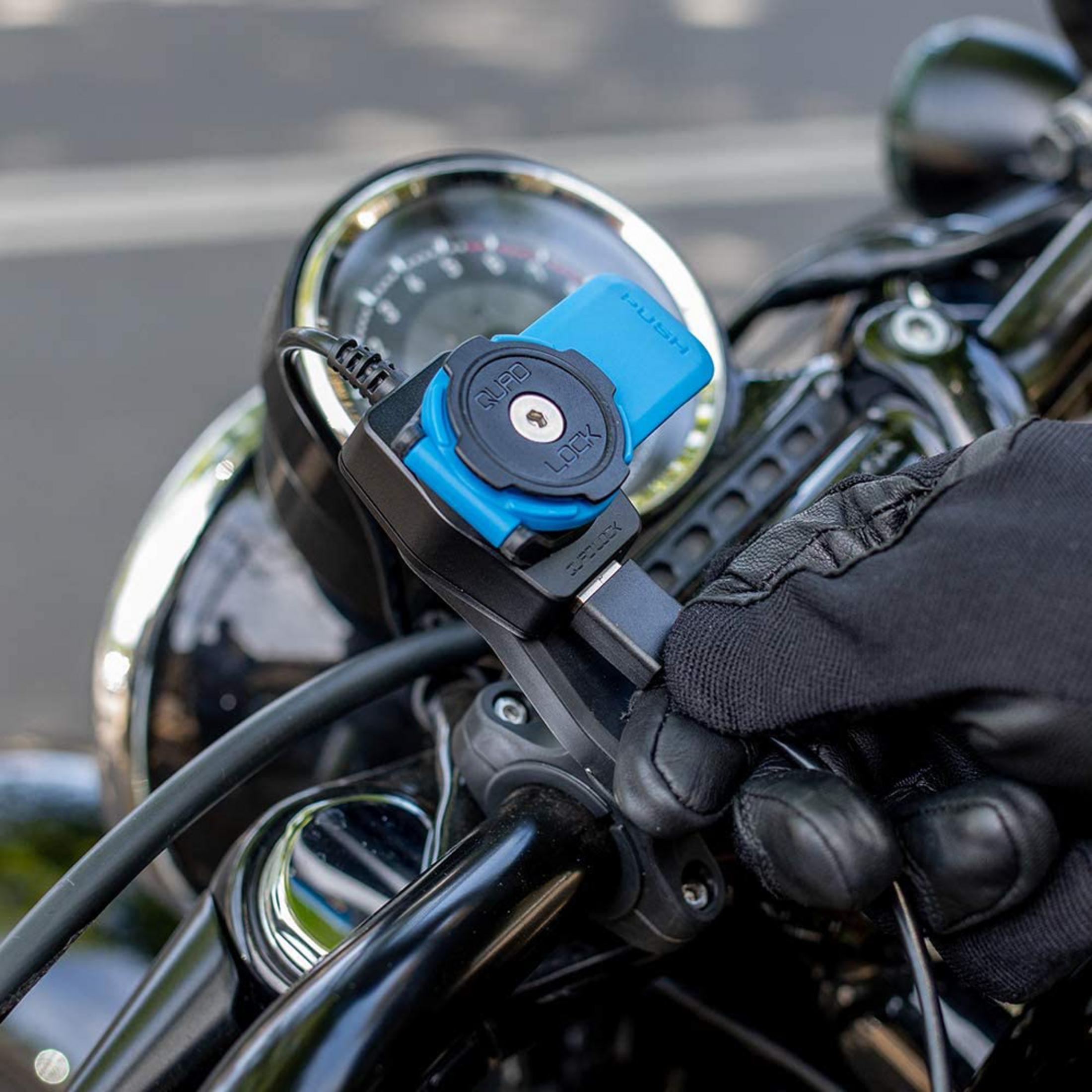 Ein blauer Quad Lock Handyhalter am Motorradlenker, daneben ein Handschuh.