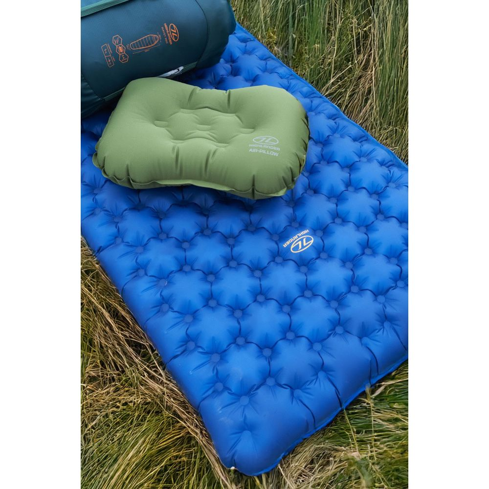Blaue Luftmatratze, grünes Kissen und grüner Schlafsack auf Gras.