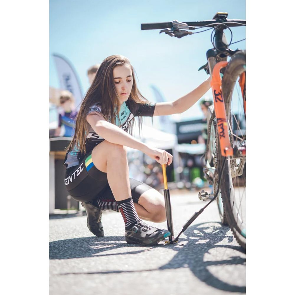 Eine junge Frau pumpt einen Mountainbike-Reifen auf. Sie kniet auf dem Boden.