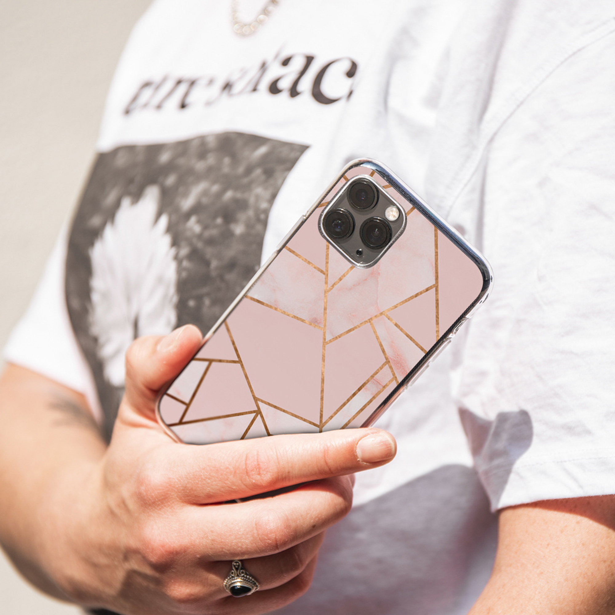 Una mano tiene uno smartphone con motivo marmorizzato rosa e linee dorate.