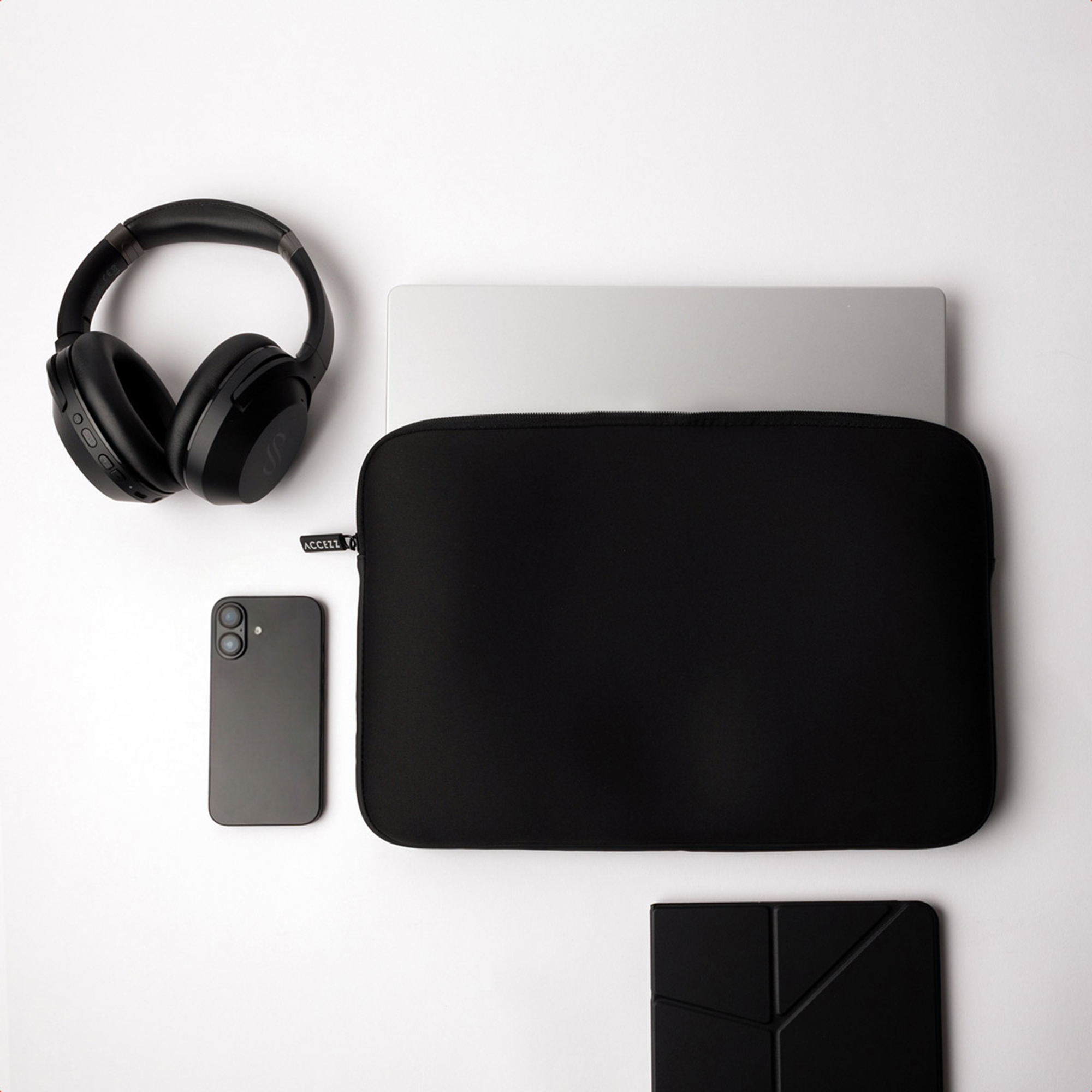 Black headphones, smartphone, laptop, and laptop sleeve on a white surface.