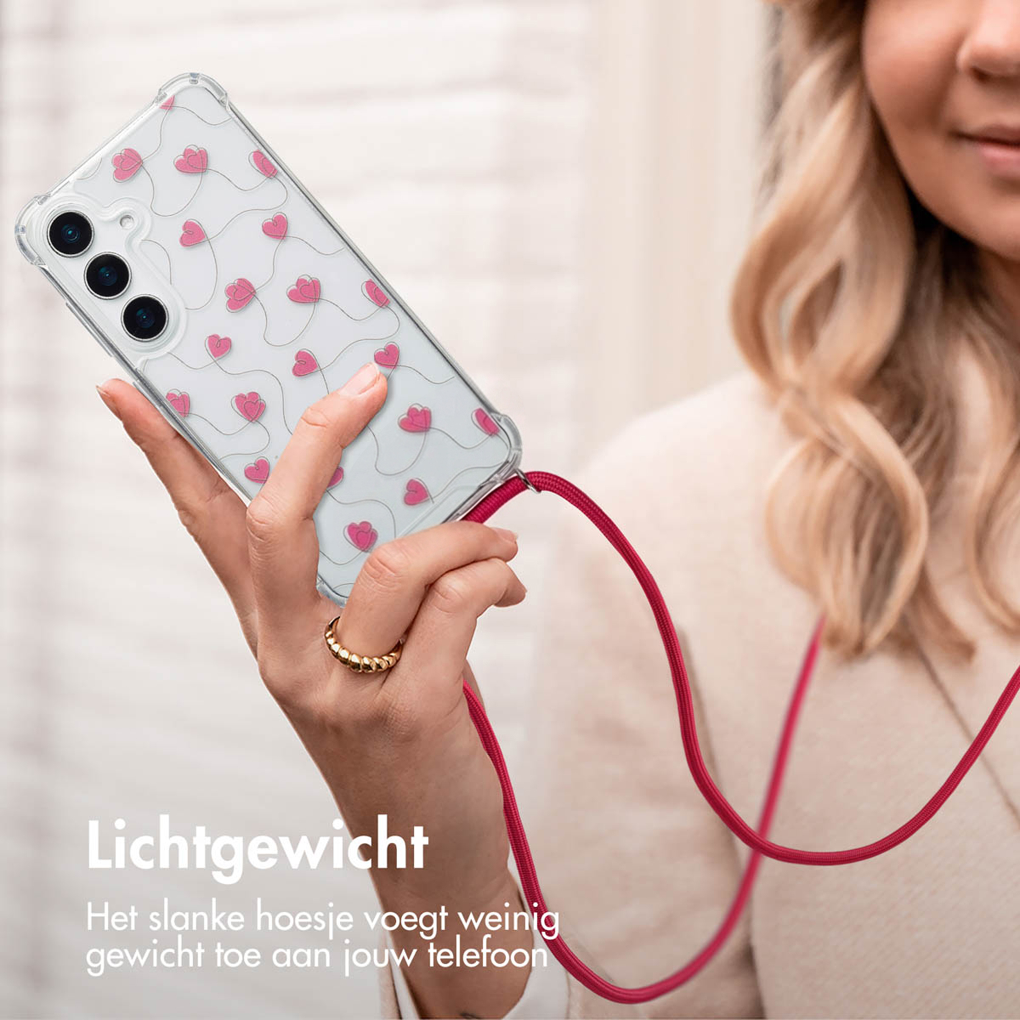 Hand met smartphone in hoesje met hartjespatroon en rood koord.