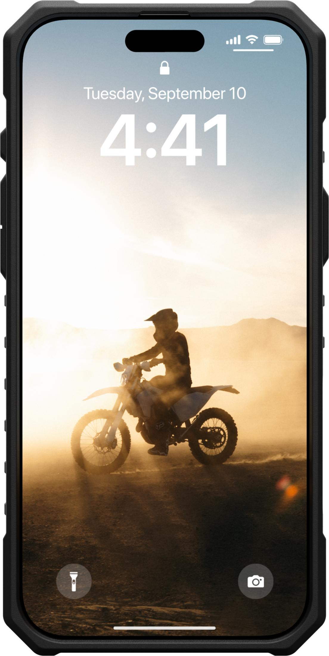 Ein Motorradfahrer reitet im Sonnenuntergang durch Staub. Berge im Hintergrund.