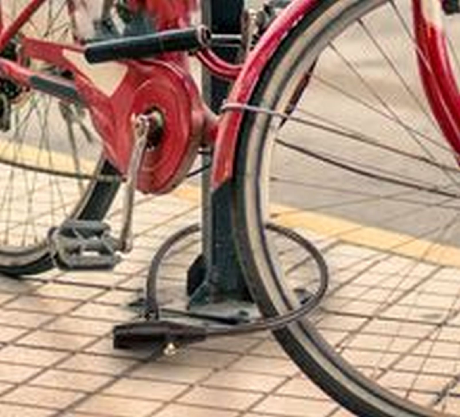 Ein rotes Fahrrad ist mit einem schwarzen Schloss an einem Pfosten angeschlossen.