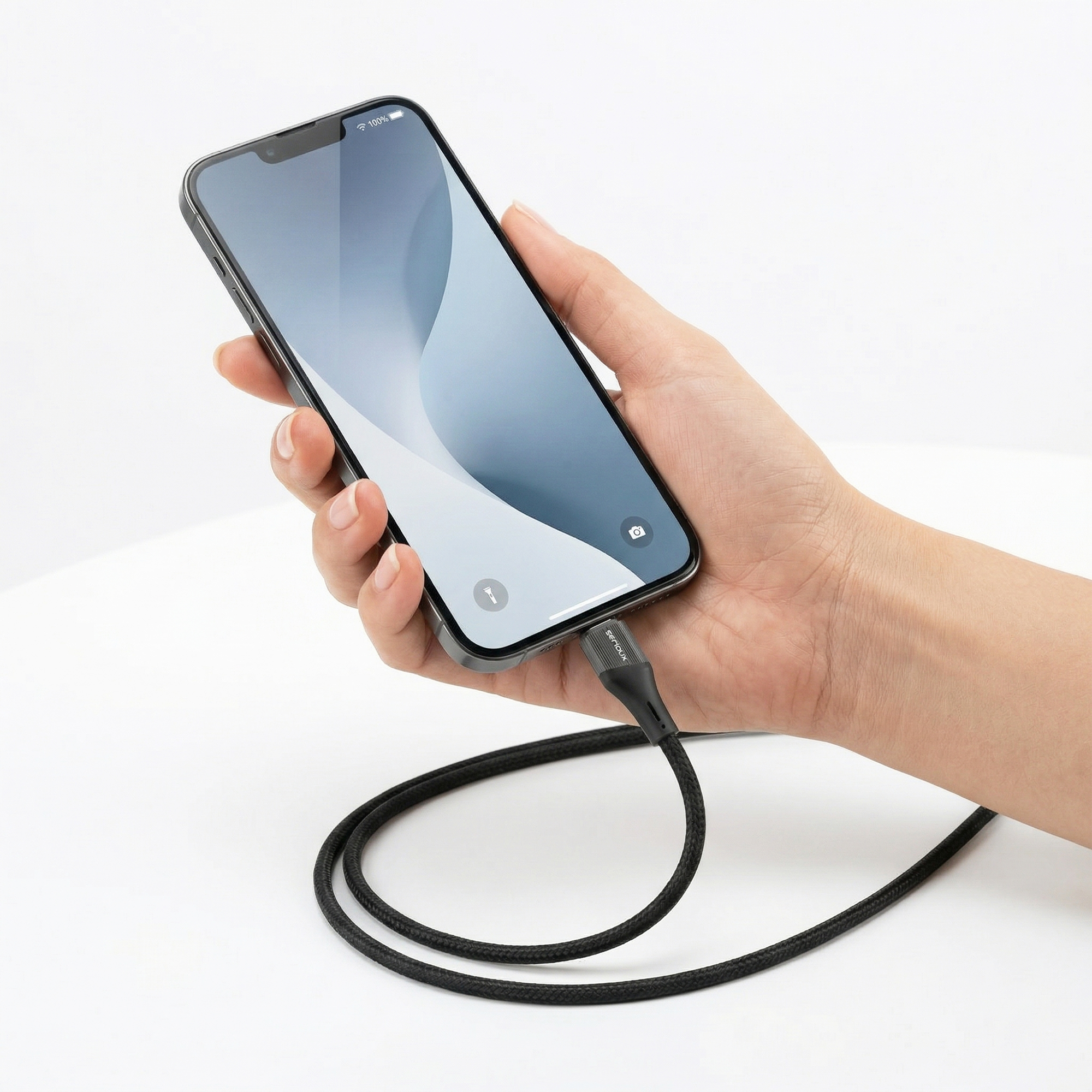 Hand die een iPhone vasthoudt met een zwarte oplaadkabel.