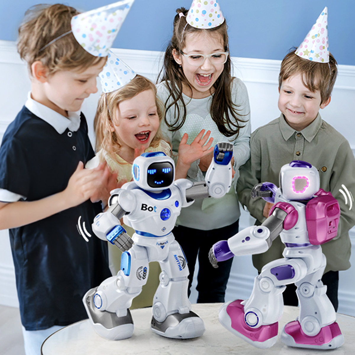 Kinder mit Partyhüten beobachten zwei tanzende Roboter auf einem Tisch.