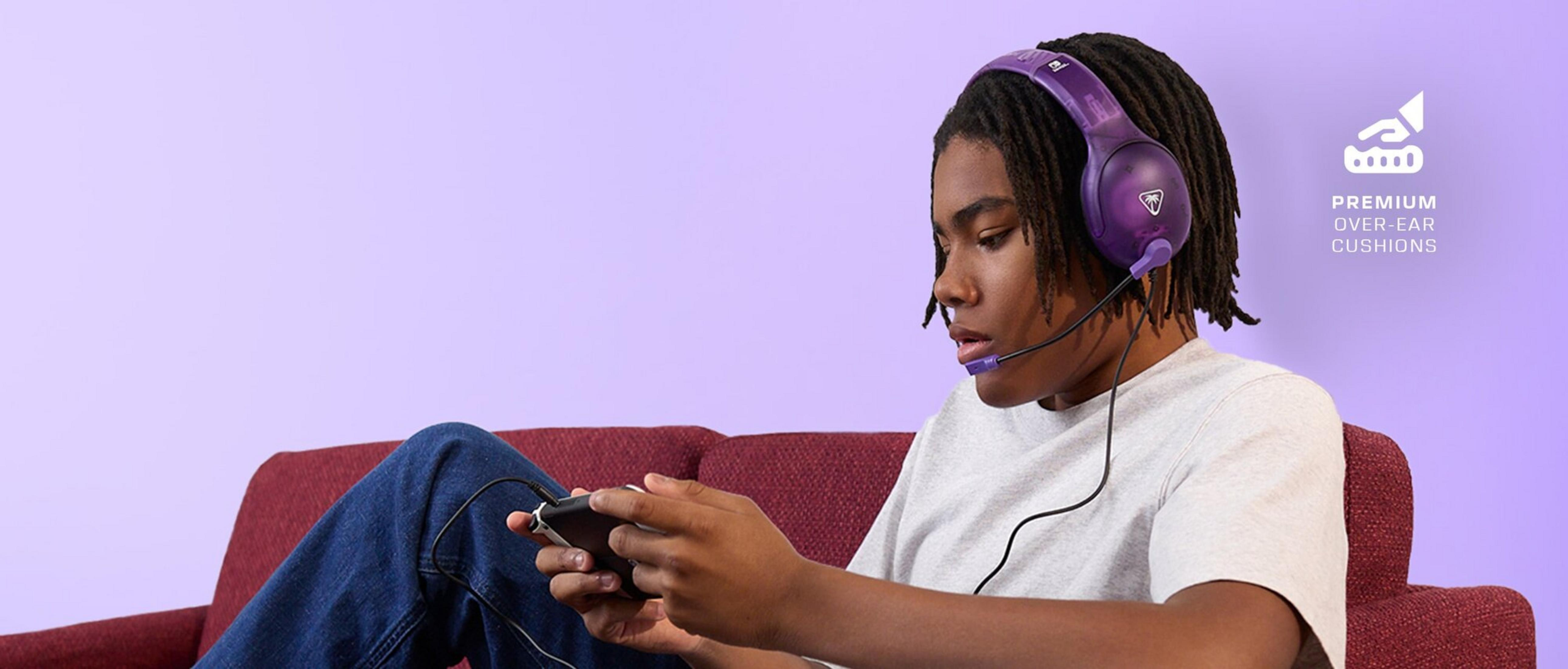 Nastolatek w fioletowych słuchawkach gra w grę mobilną na czerwonej kanapie.