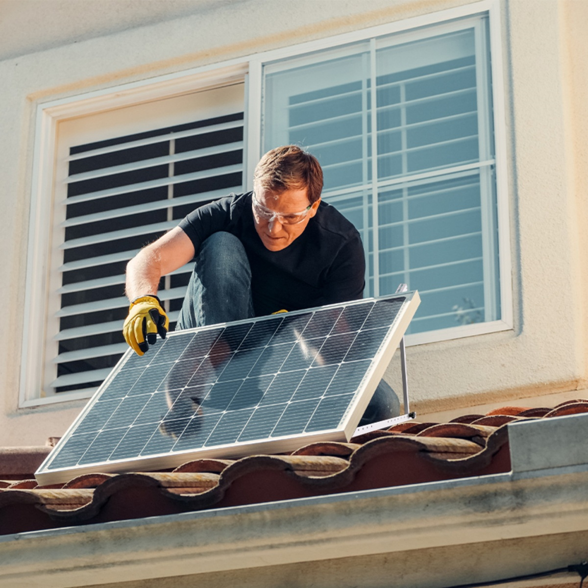 Ein Mann mit Handschuhen installiert ein Solarpanel auf einem Dach.