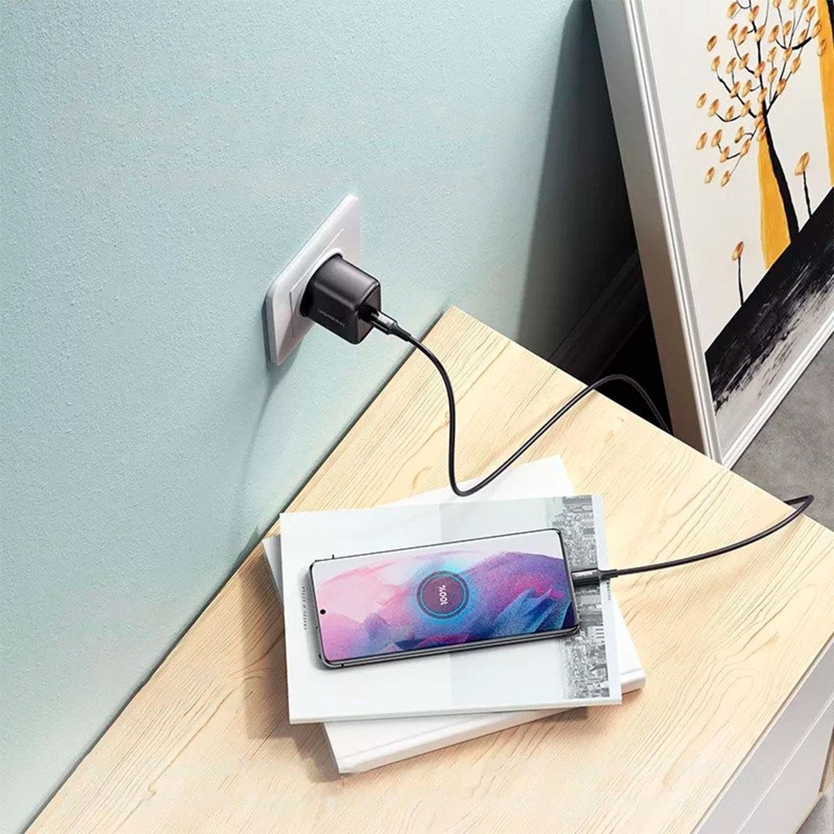 Czarna ładowarka podłączona do gniazdka ściennego ładuje smartfon leżący na książkach.