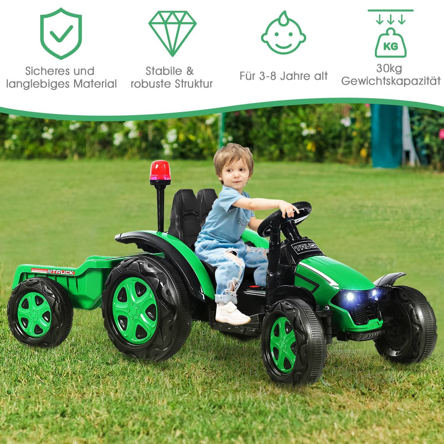 A boy rides a green toy tractor with a trailer on grass.