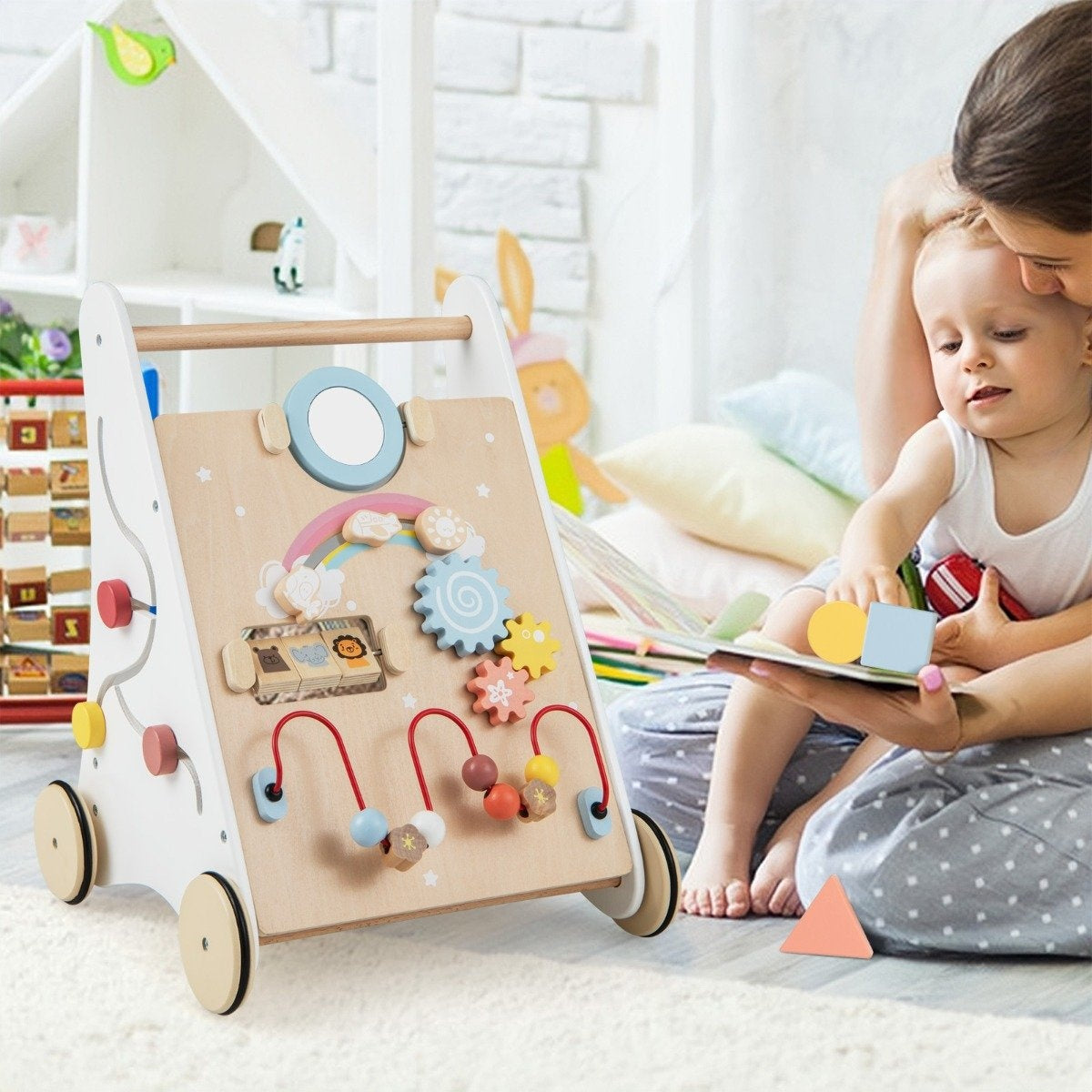 A baby sits with an adult, looking at a book. A wooden activity walker is in the foreground.