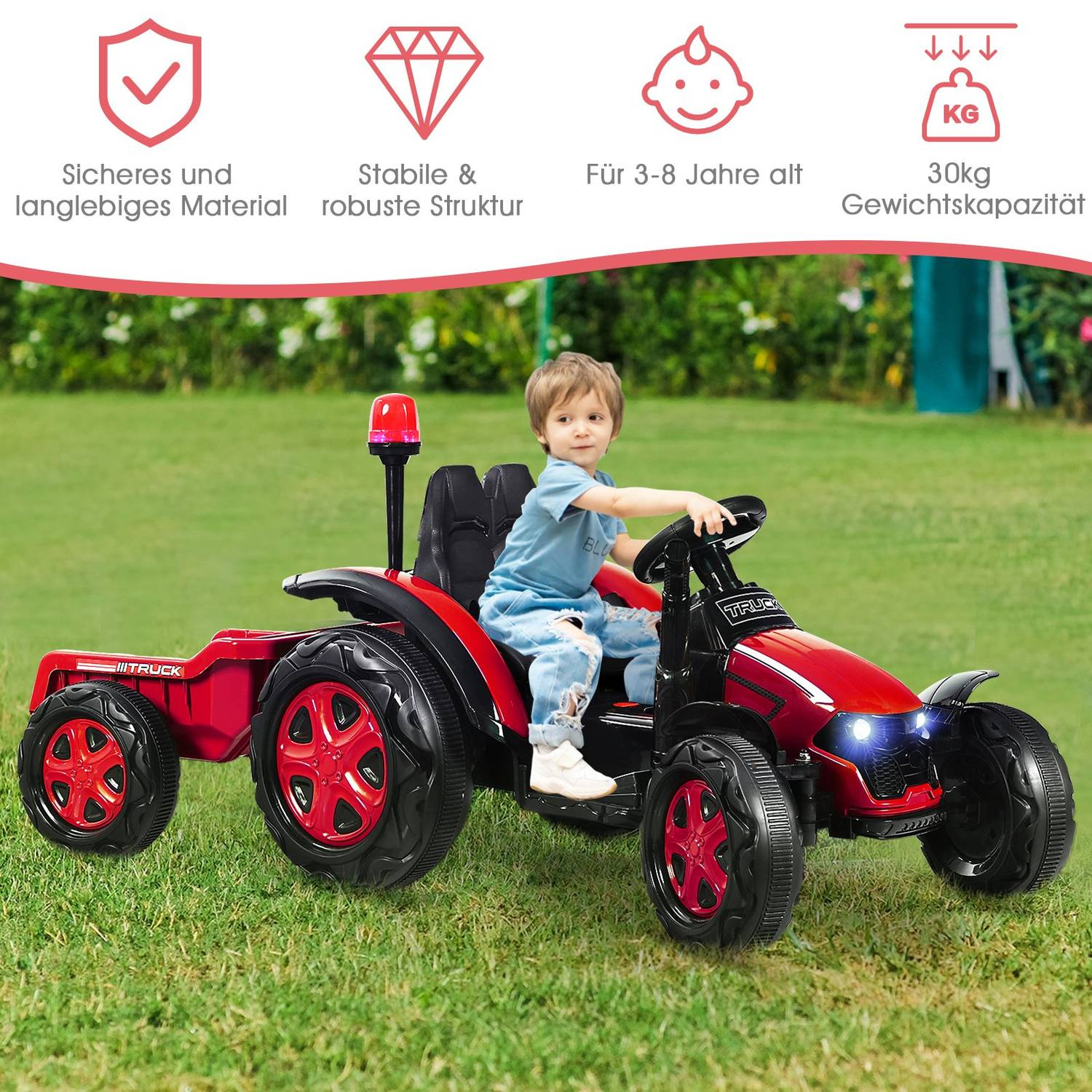 A boy rides a red toy tractor with a trailer on green grass.