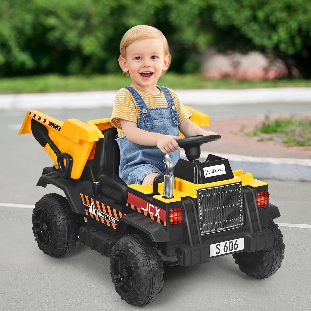 A toddler sits in a yellow and black toy dump truck on a road.