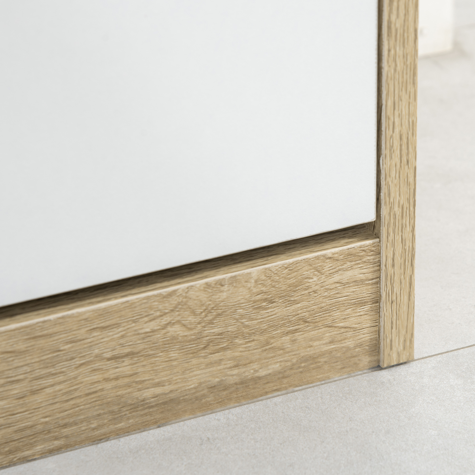 Primer plano de superficie blanca con moldura de madera y baldosas.