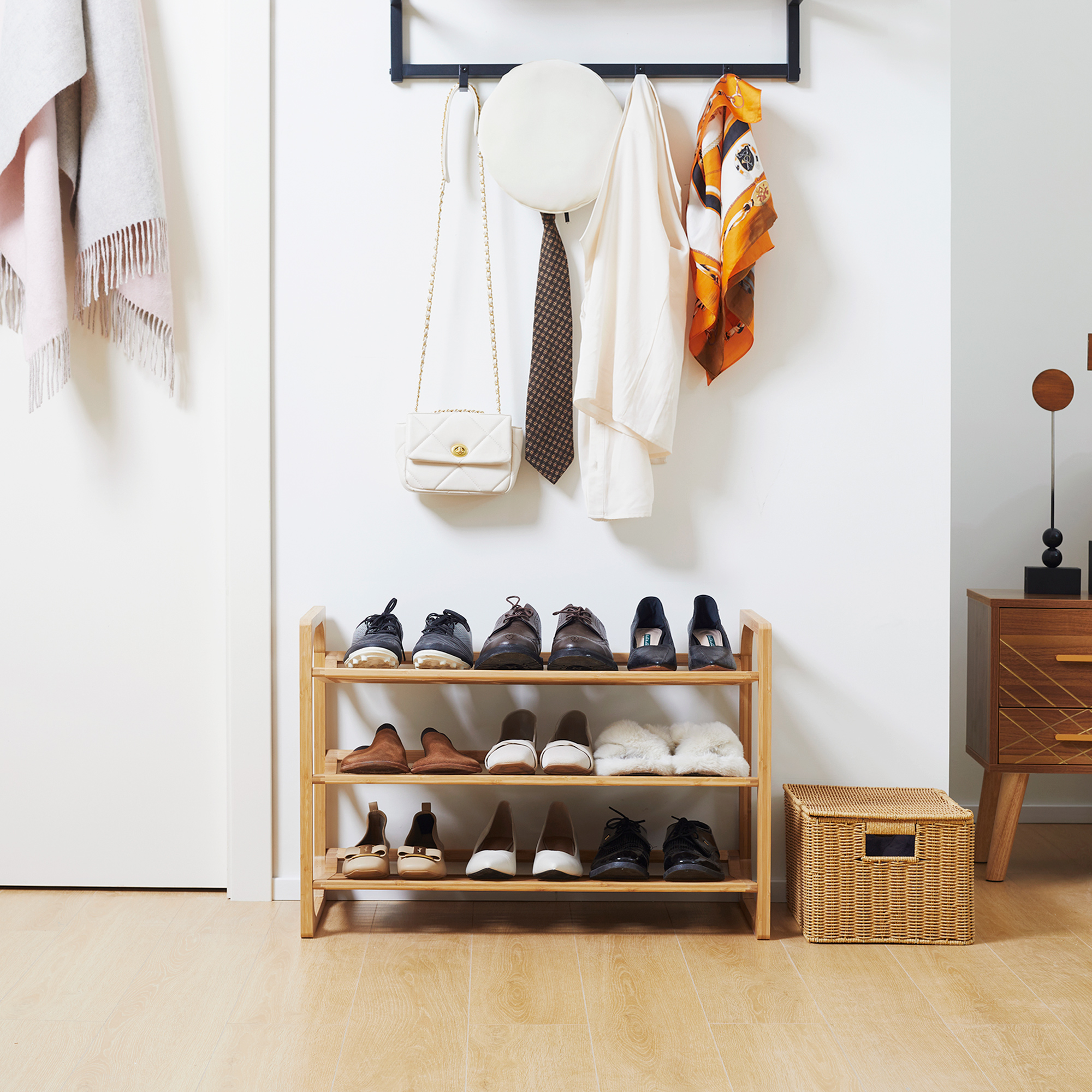 Un zapatero de madera con zapatos, un bolso blanco y ropa colgada en la pared.