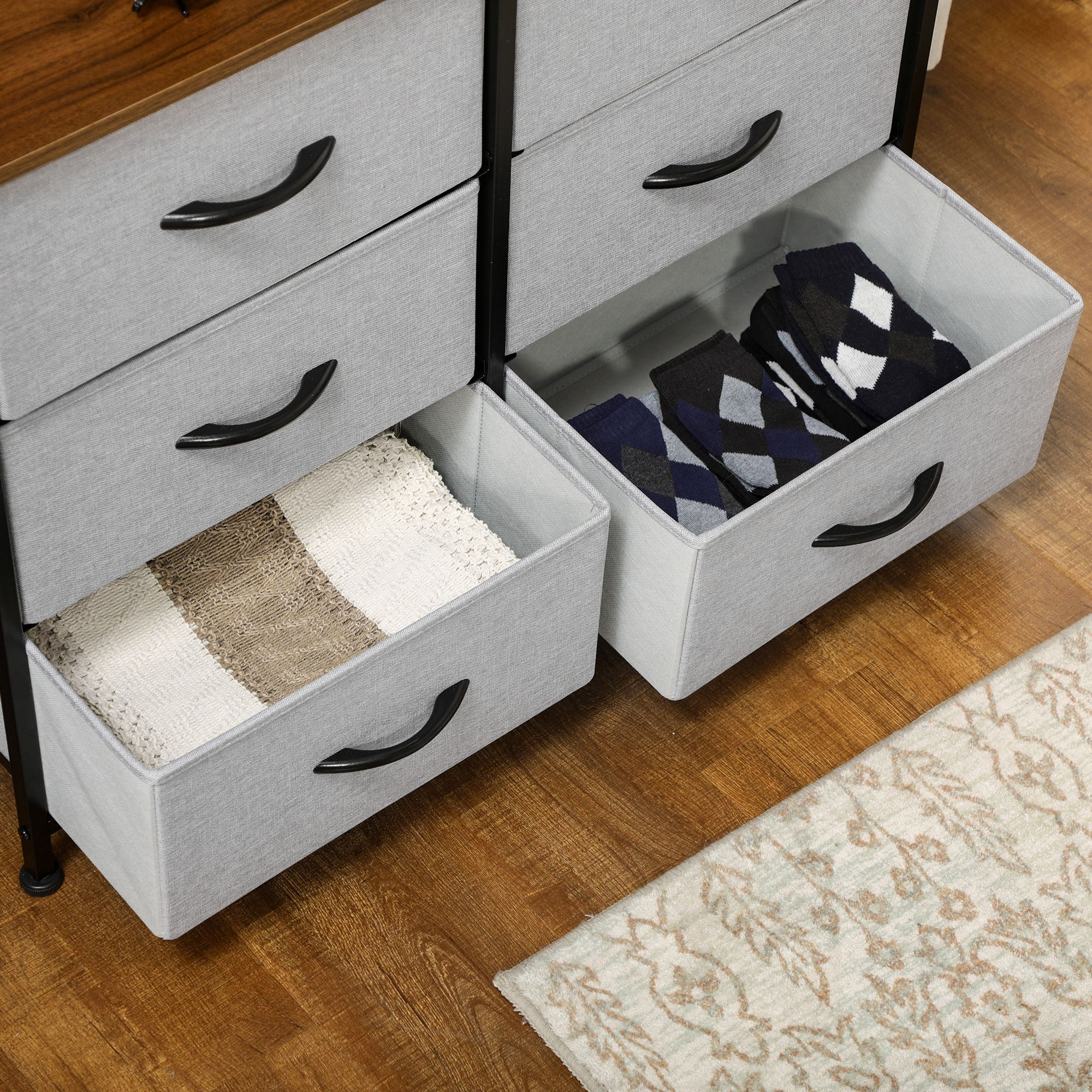 Detalle de cómoda de tela gris con cajones abiertos con calcetines y manta.