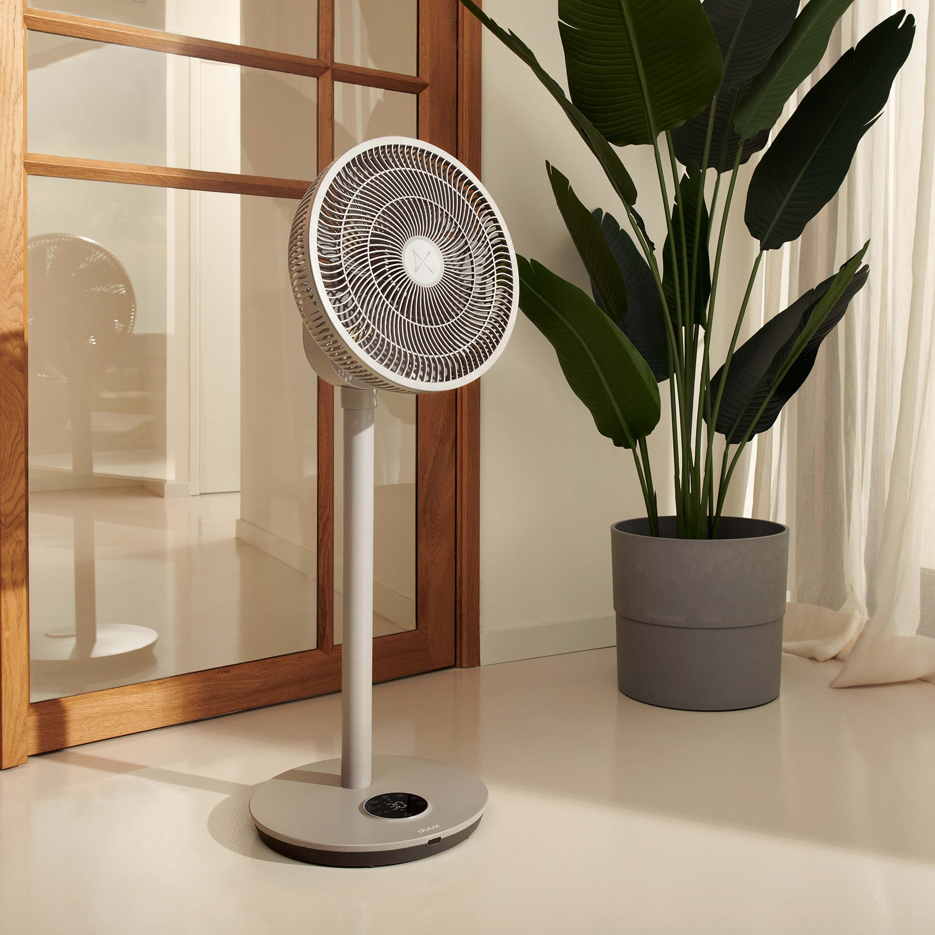 Un ventilateur sur pied blanc est placé à côté d'une grande plante en pot verte.