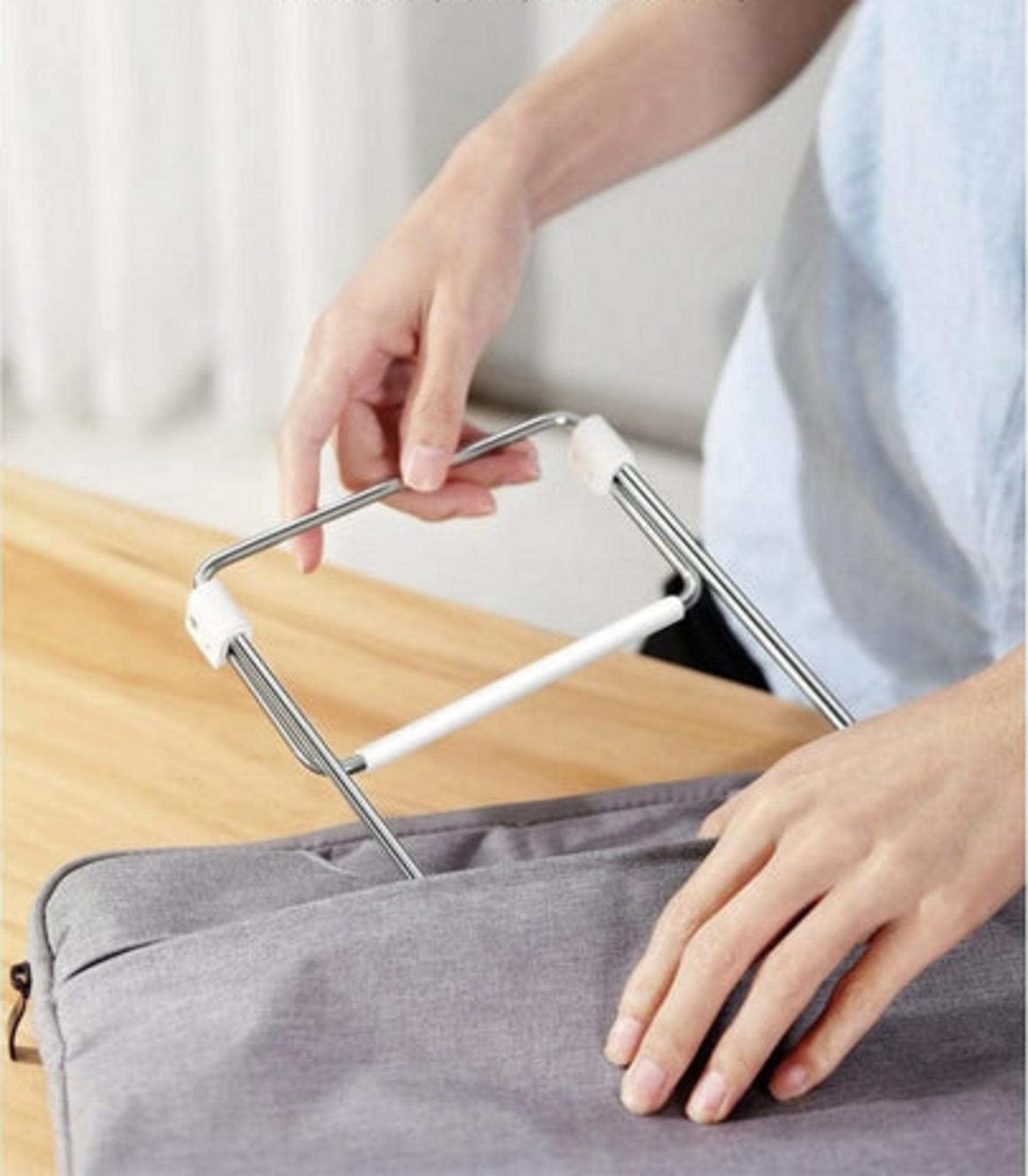 Ręce składające metalowy wieszak na ubrania nad szarą torbą na drewnianym stole.