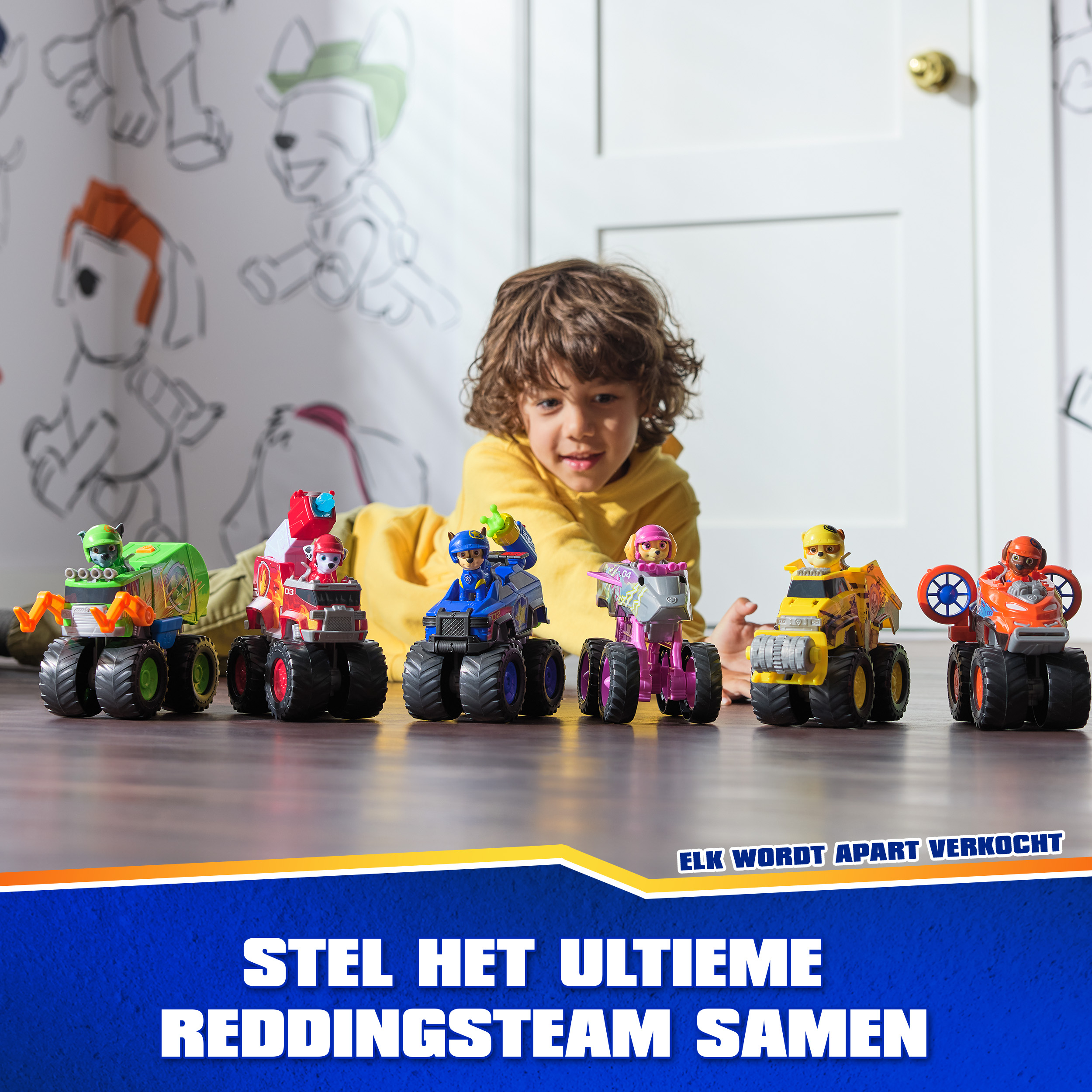 Un niño juega con seis monster trucks de Paw Patrol frente a una puerta con arte mural.