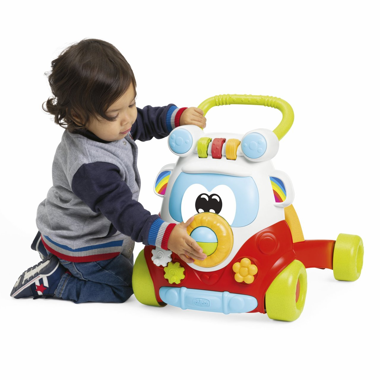 Un niño pequeño se arrodilla jugando con un andador de coche de juguete colorido. El niño lleva vaqueros y un jersey gris.