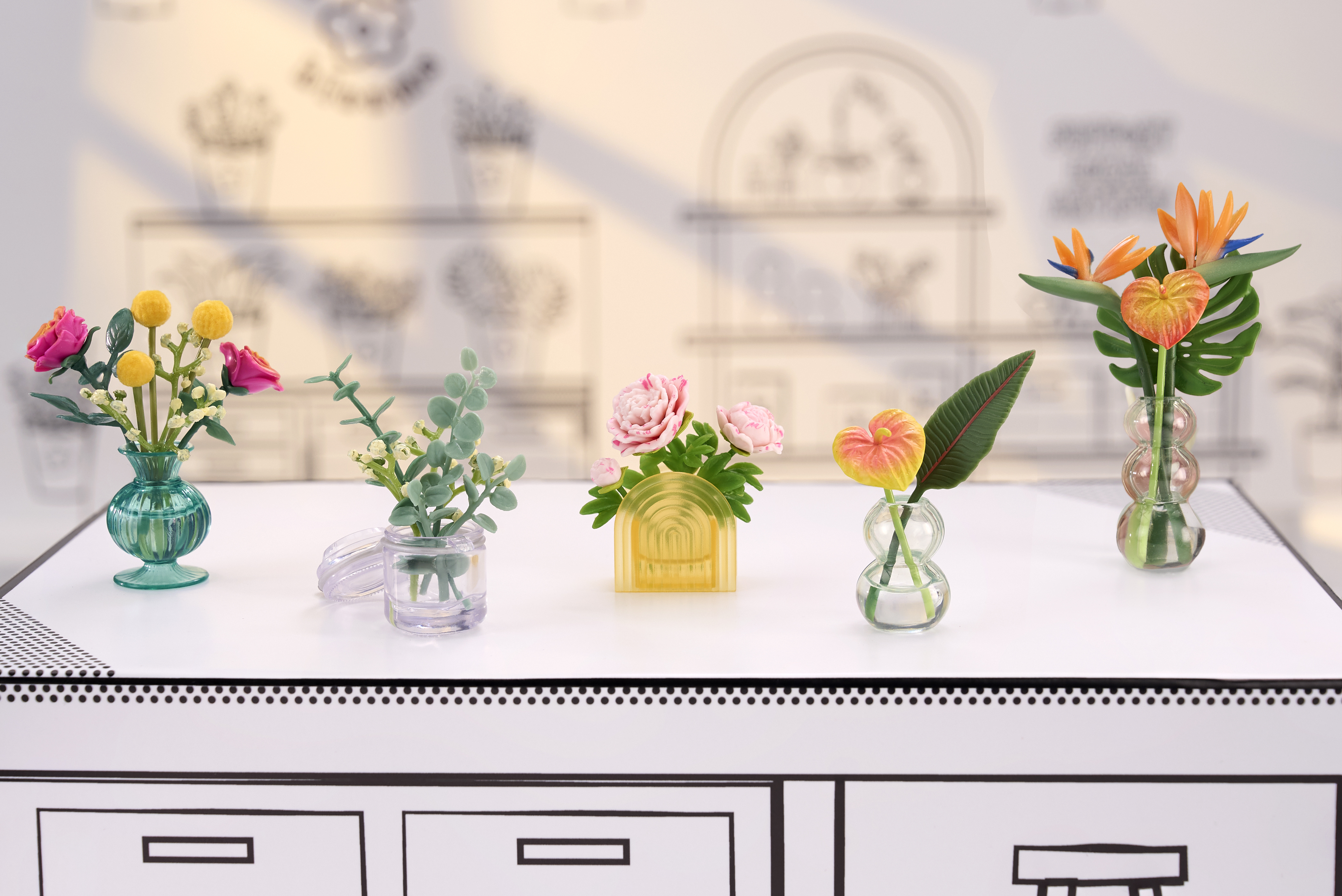 Cinque mini vasi con fiori e foglie colorate disposti su una superficie bianca.