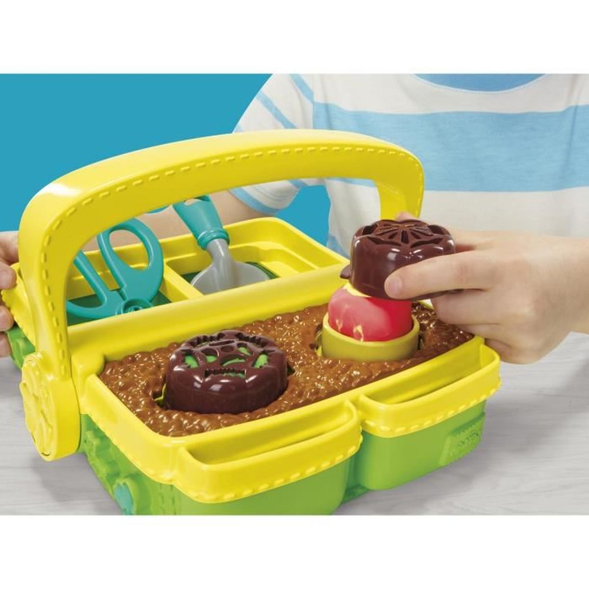 Un niño juega con un juego de herramientas de jardinería de plástico en una caja.