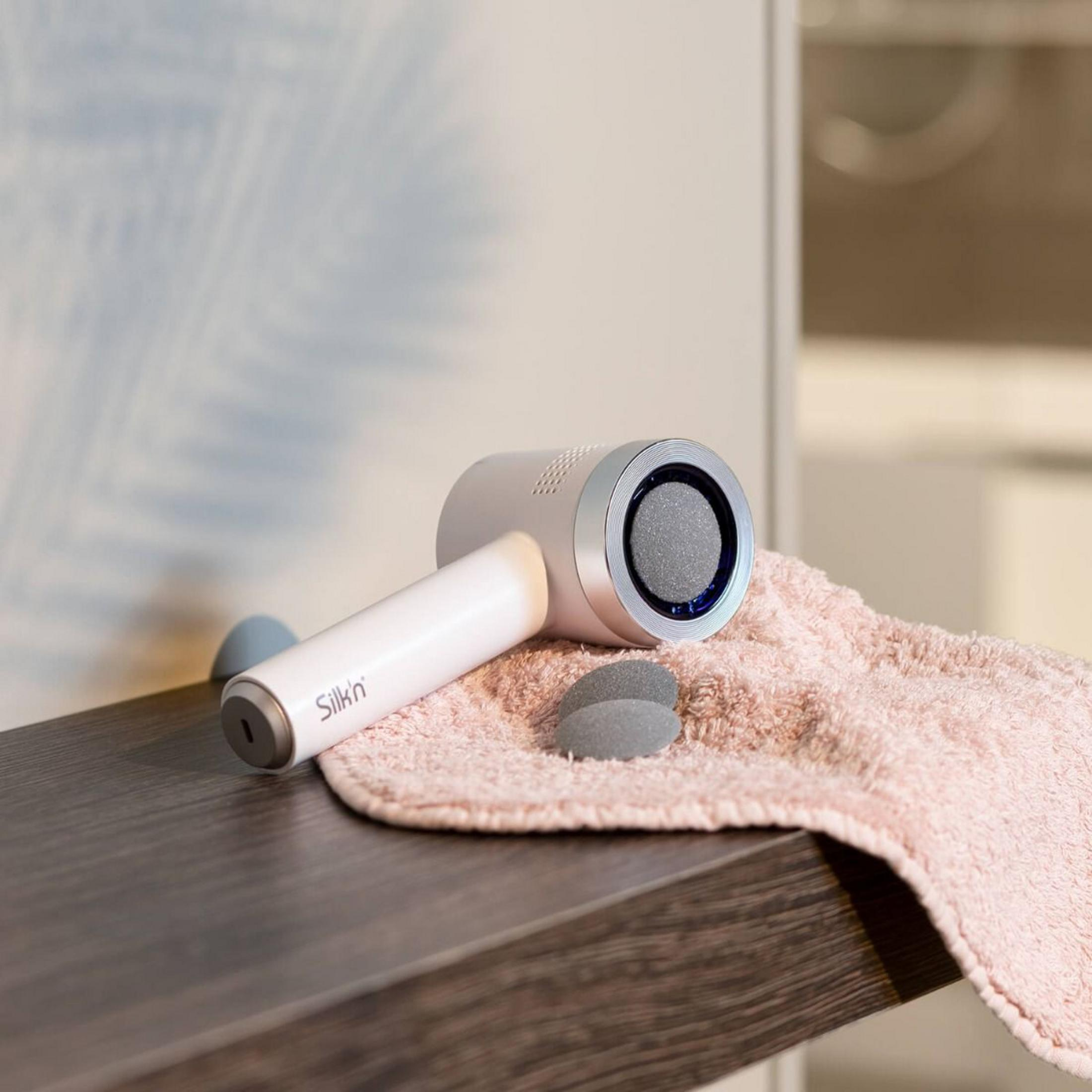 Biały elektryczny usuwacz zrogowaceń leży na różowym ręczniku.