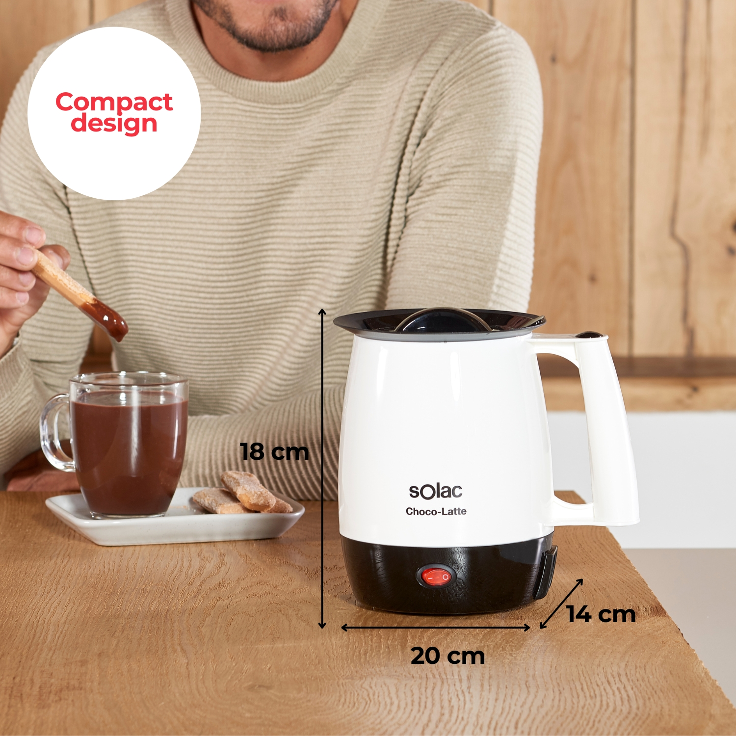 Un hombre moja un palo de madera en chocolate caliente. Un aparato está junto a una taza.
