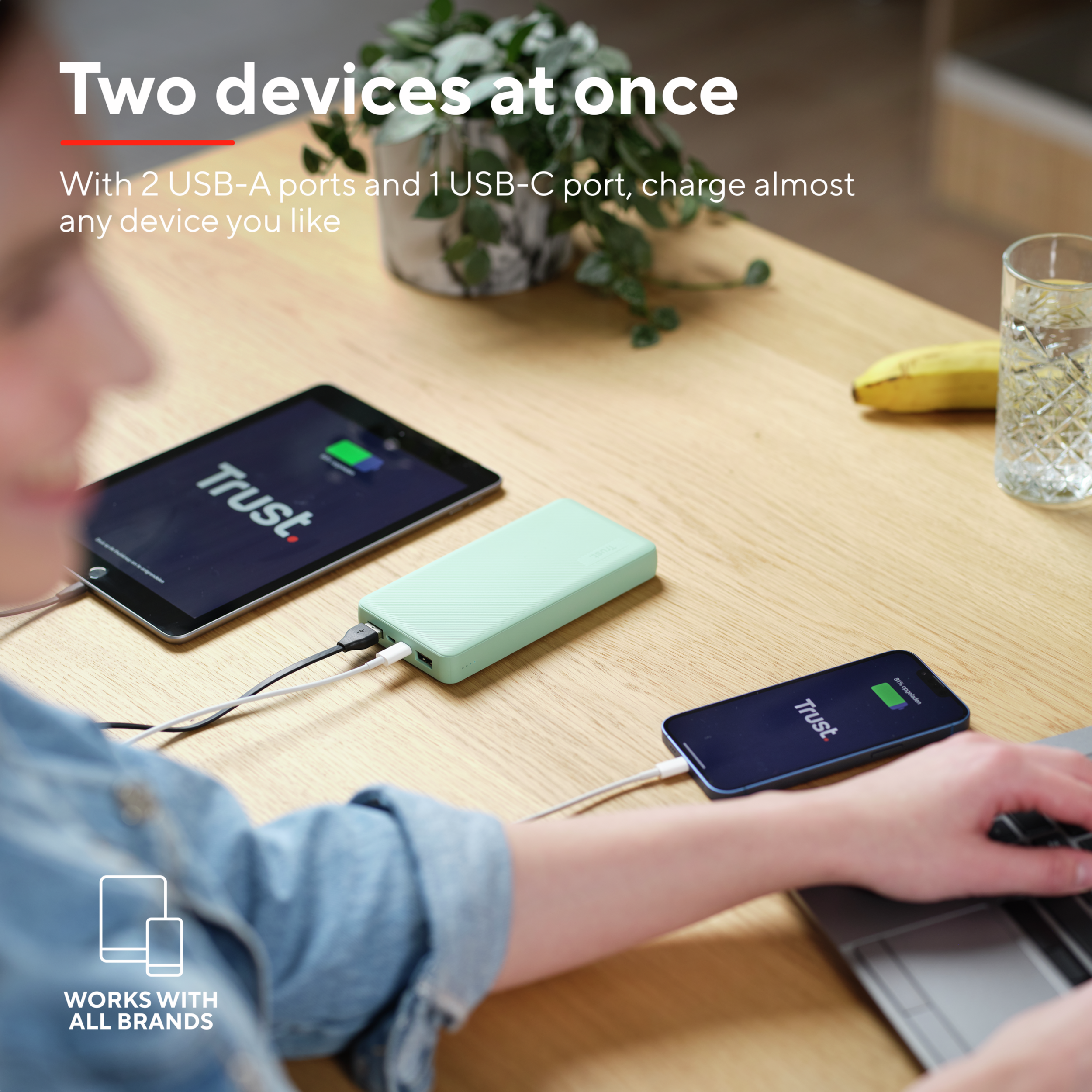 Un power bank verde carica un tablet e uno smartphone su un tavolo di legno.